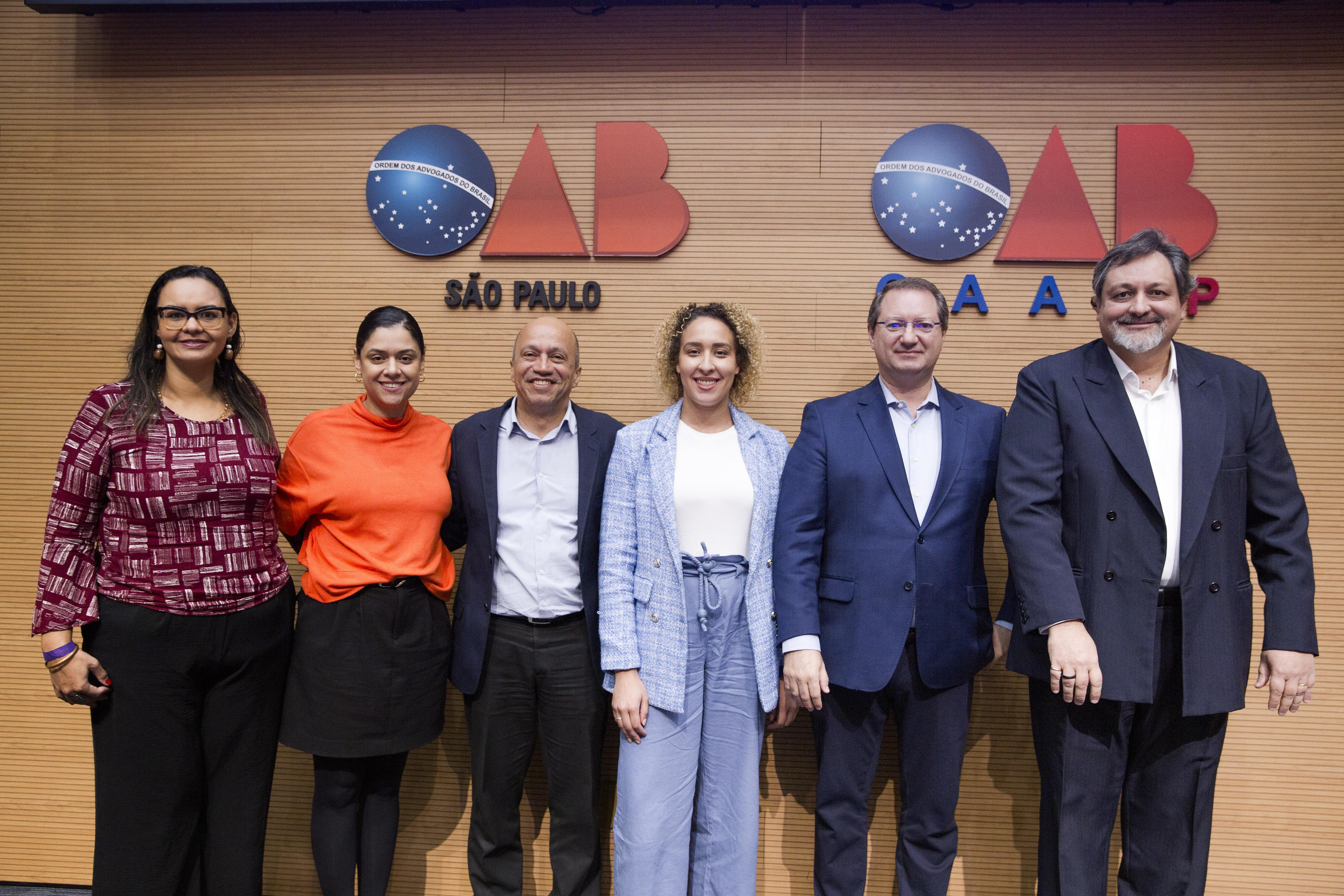 Grupo de seis pessoas a frente de painel com símbolos escritos OAB São Paulo e OAB Caasp.